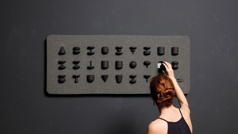 Frau vor einer schwarzen Tafel mit erhobenen Buchstaben. 