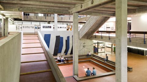 Innenraum des Fachbereichs Architektur an der TU Darmstadt Innenraum des Fachbereichs Architektur der TU Darmstadt mit mehreren Ebenen und Treppen. Dan den Wänden sind gerahmte Kunstwerke zu sehen.