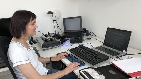 Sabine Lohner mit kurzem T-Shirt am Schreibtisch sitzend, arbeitet an ihrem Rechner.